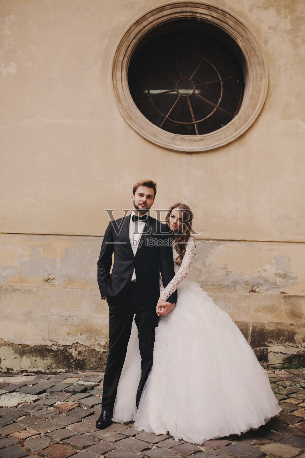 时尚的新娘和新郎在欧洲城市的街道上轻轻拥抱。华丽的新婚夫妇在古建筑附近拥抱。浪漫的时刻。结婚的那一天照片摄影图片