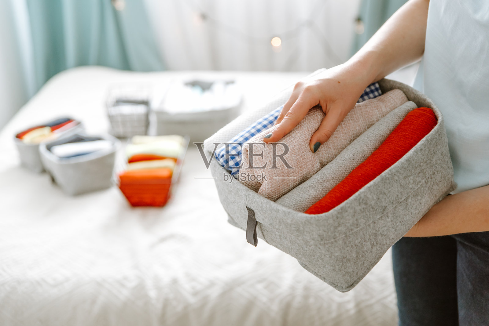 女人把衣服整理在衣柜里，把衬衫放进盒子里，把篮子放进架子上。衣服洗好后叠整齐。简约生活方式的概念照片摄影图片