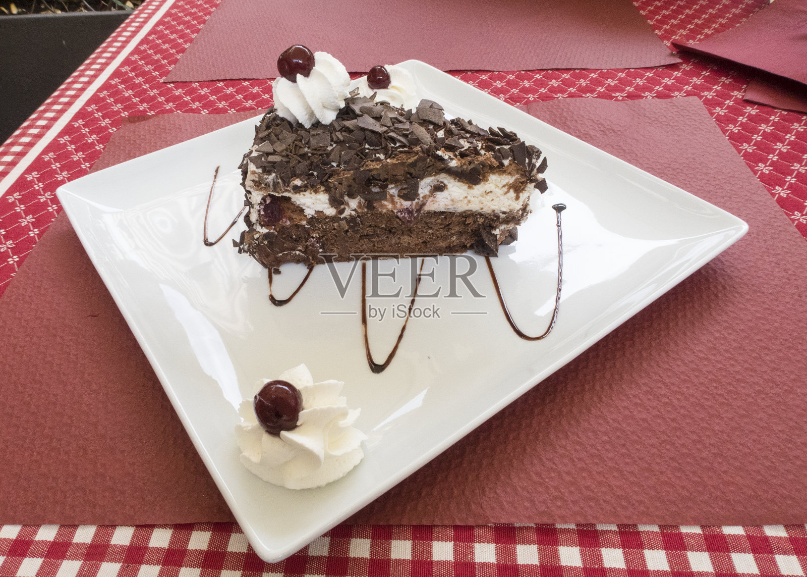 桌子上白色的盘子上放着一片黑森林蛋糕照片摄影图片
