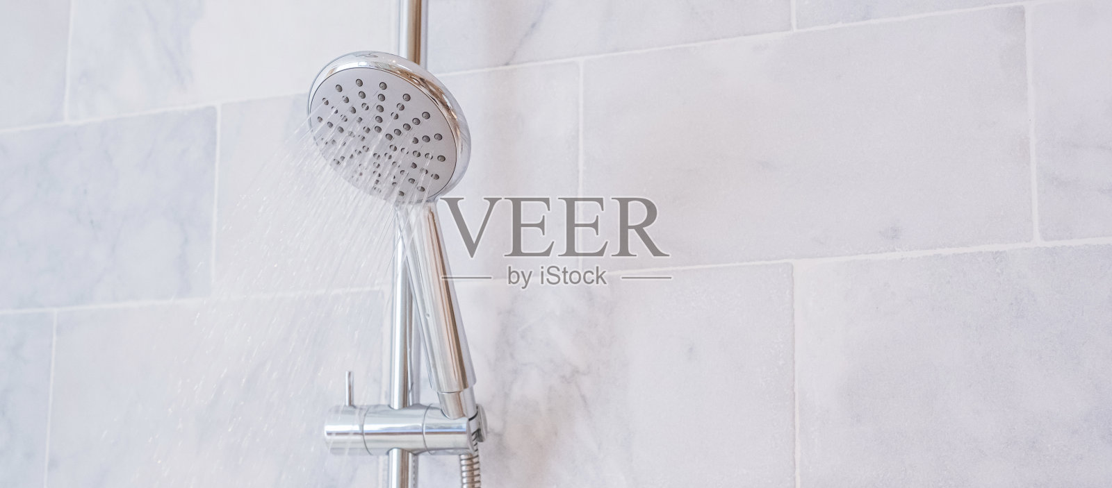 在现代浴室中，大理石墙背景下的淋浴喷头和水龙头喷出的水滴照片摄影图片