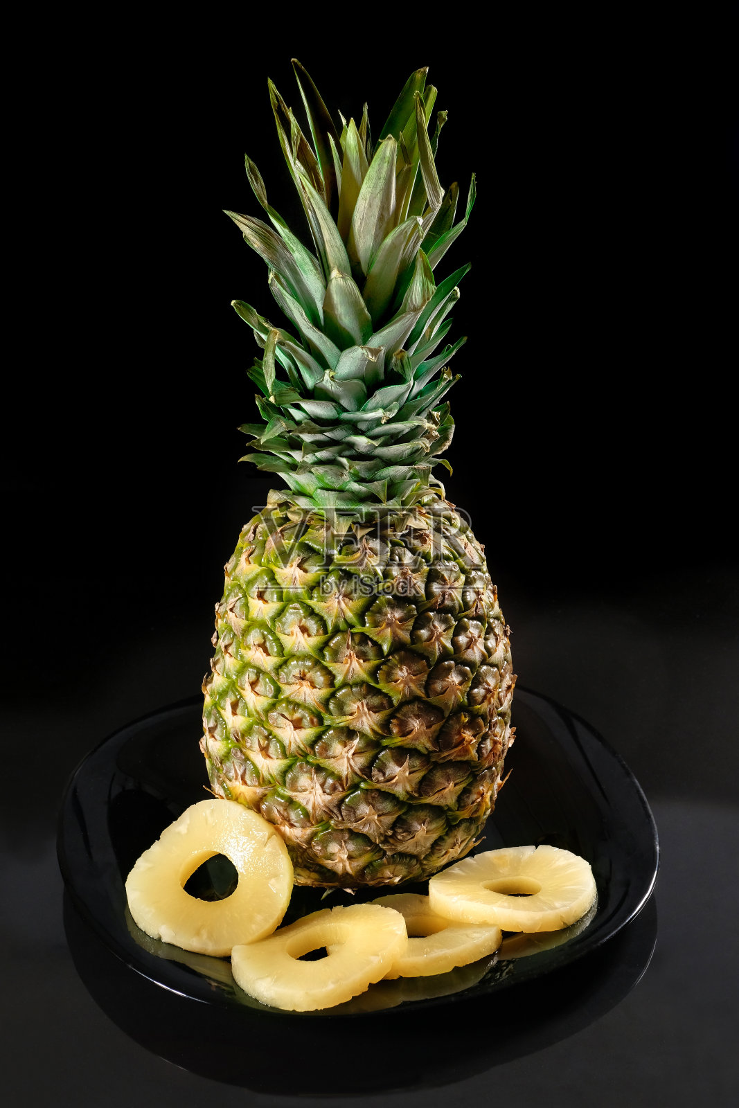 菠萝和菠萝切片放在一个黑色的盘子，在一个黑色的背景。照片摄影图片