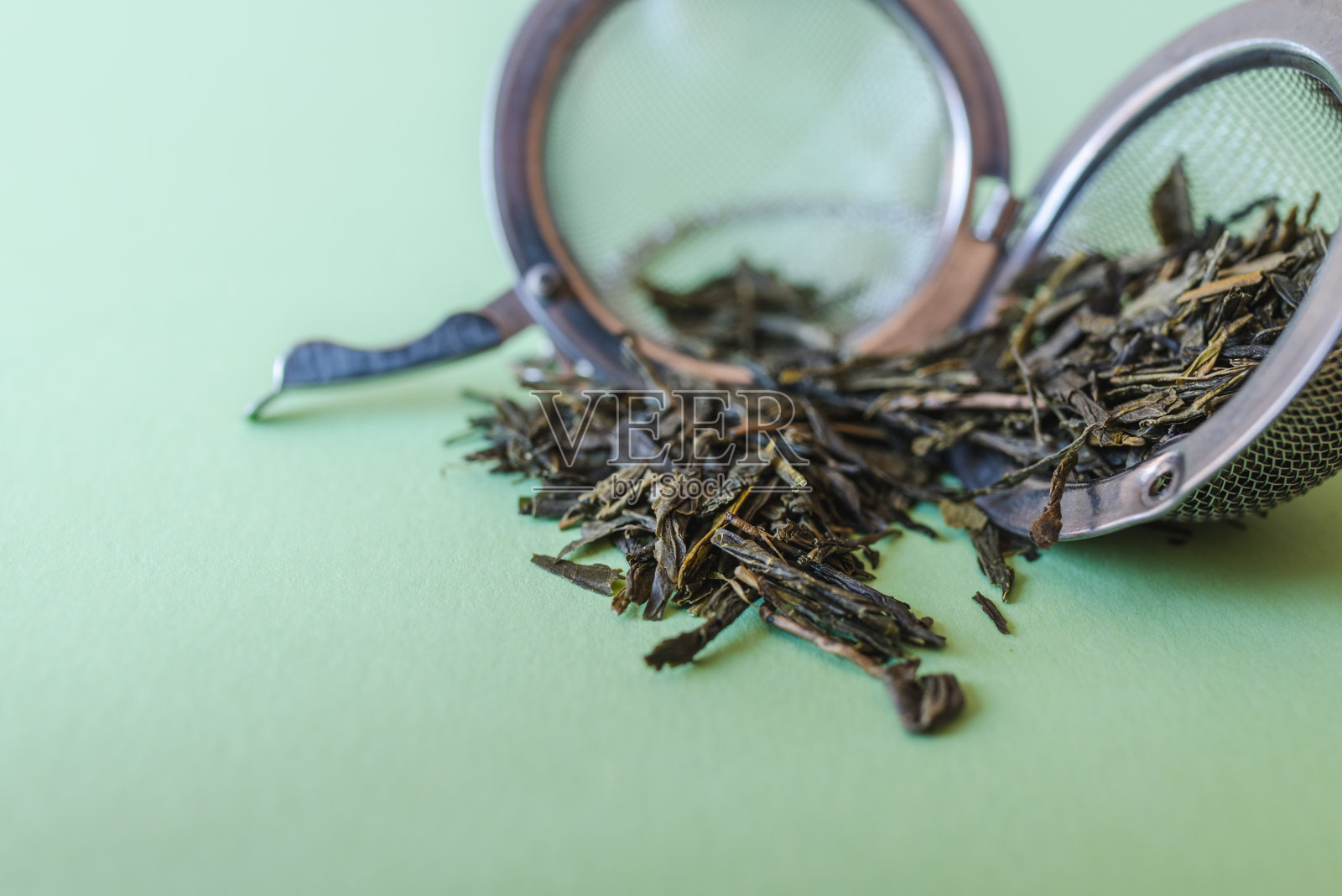 近距离观察浅绿色的桌子表面与一个开放的茶叶过滤器和干茶叶在顶部照片摄影图片