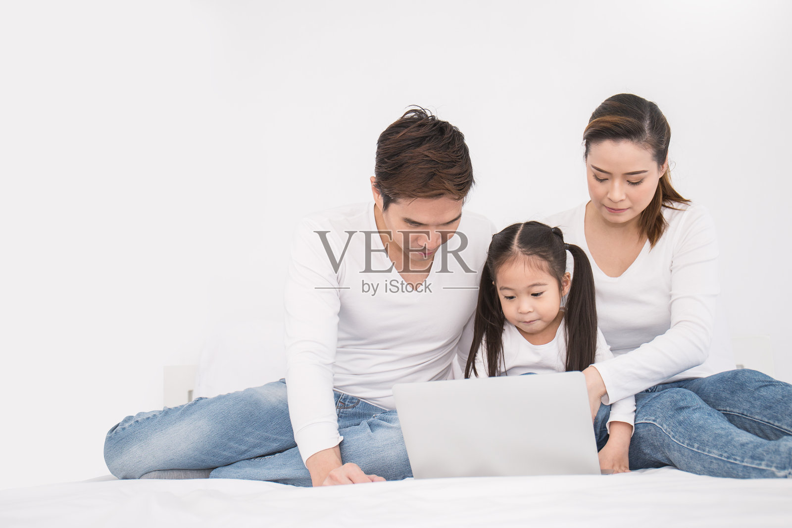 亚洲家庭躺在床上看平板电脑的肖像，亚洲小女孩和她的父母使用笔记本电脑。周末假期休闲时光教育理念照片摄影图片