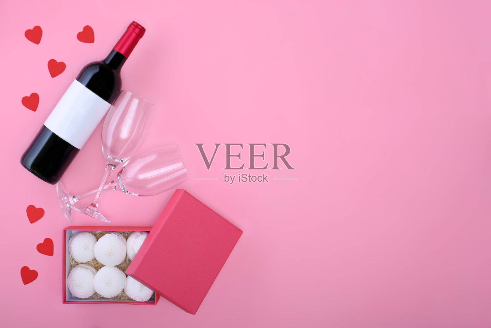 情人节贺卡。粉红色背景上的红酒配酒杯和礼品盒。俯视图照片摄影图片