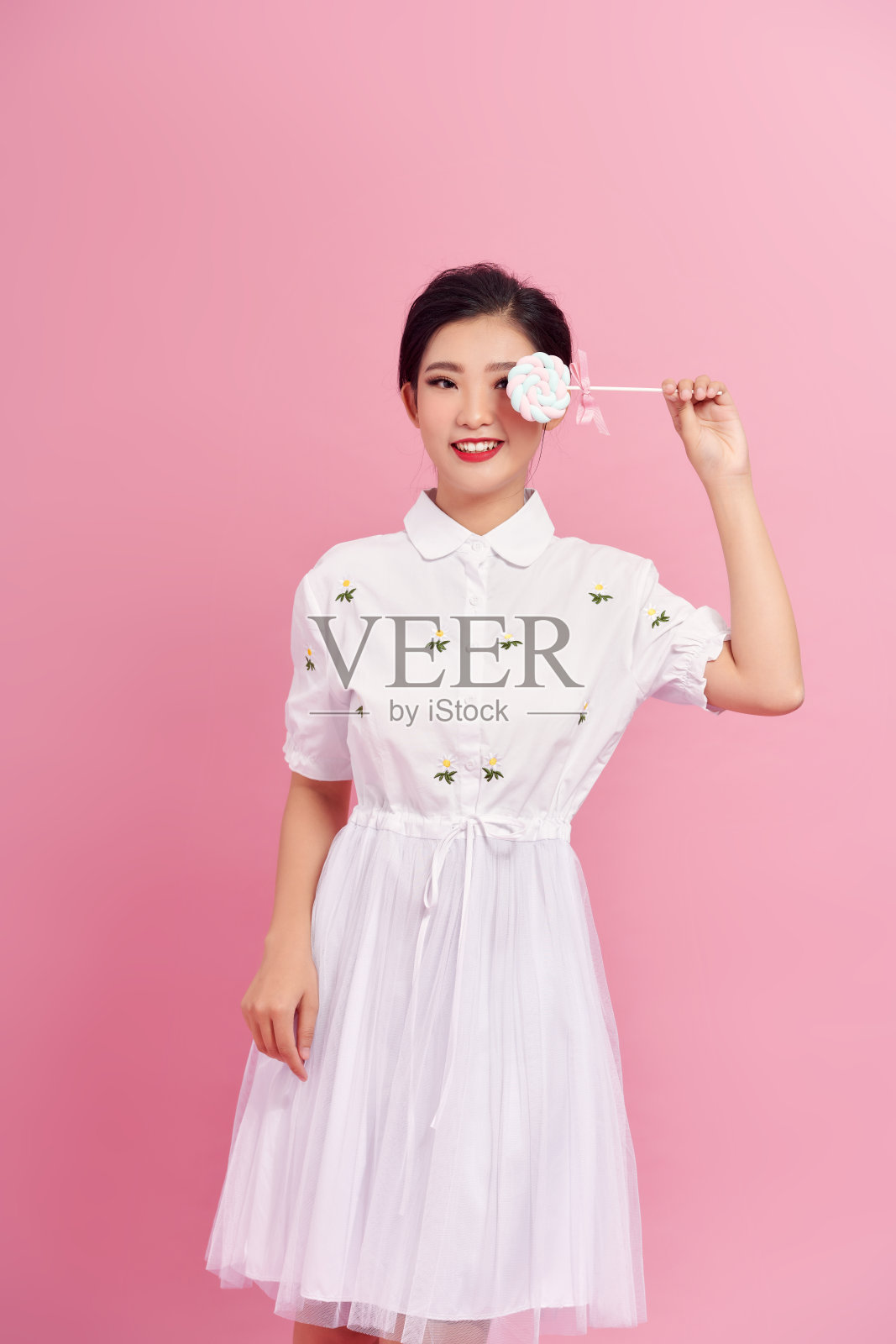 可爱的女孩用一根大棒棒糖遮住她的眼睛照片摄影图片