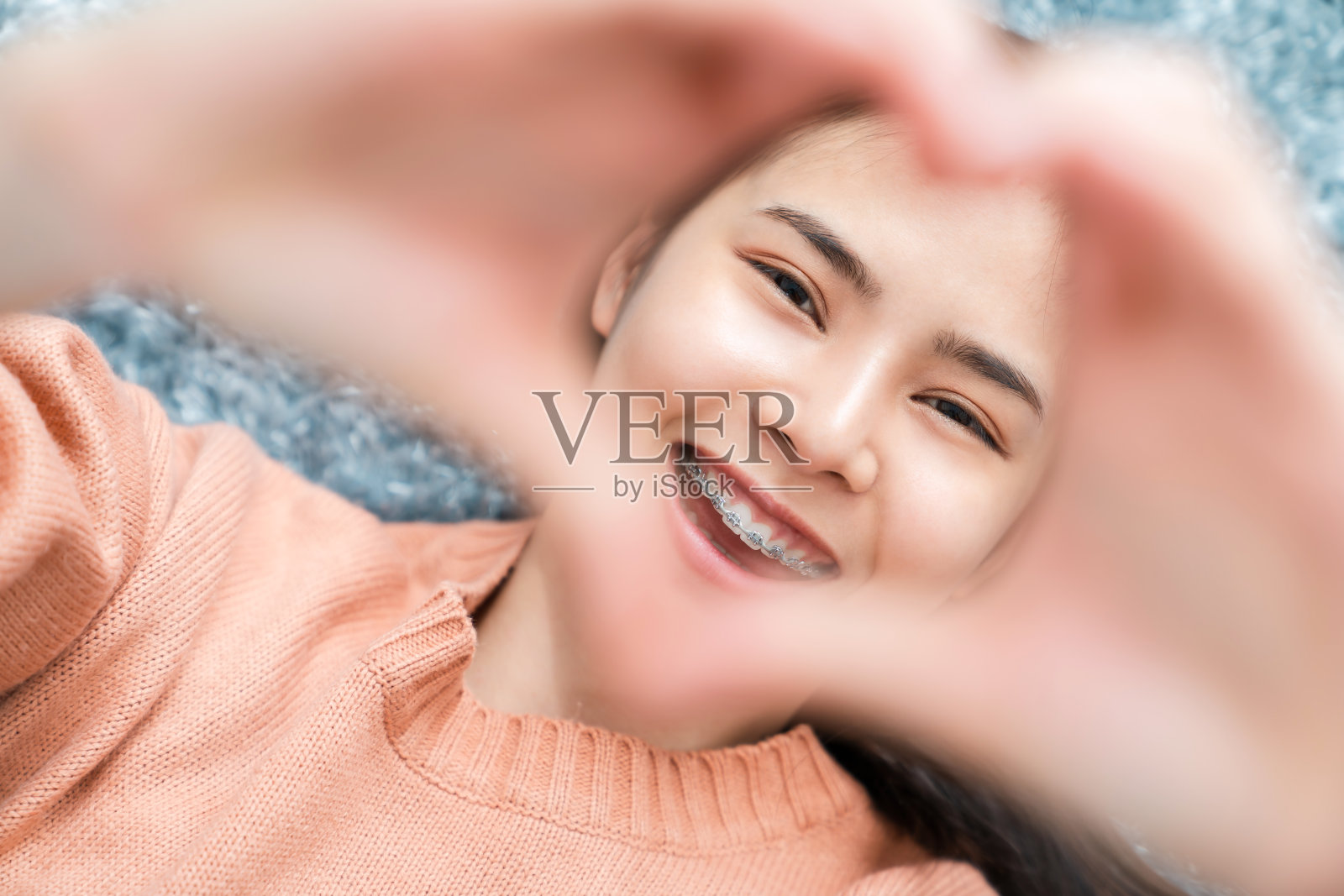 一个快乐美丽的亚洲女人在一个橙色的衬衫躺在地板上和手触摸相机在家里。照片摄影图片