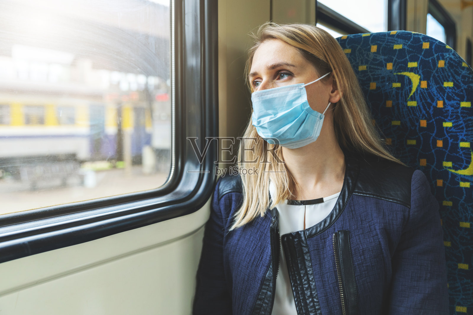 戴着安全面罩的妇女坐在火车上，从窗户往外看。病毒大流行照片摄影图片