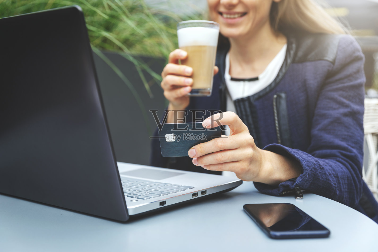 微笑的女人手里拿着信用卡，在咖啡馆喝咖啡时使用笔记本电脑。网上购物和支付概念照片摄影图片