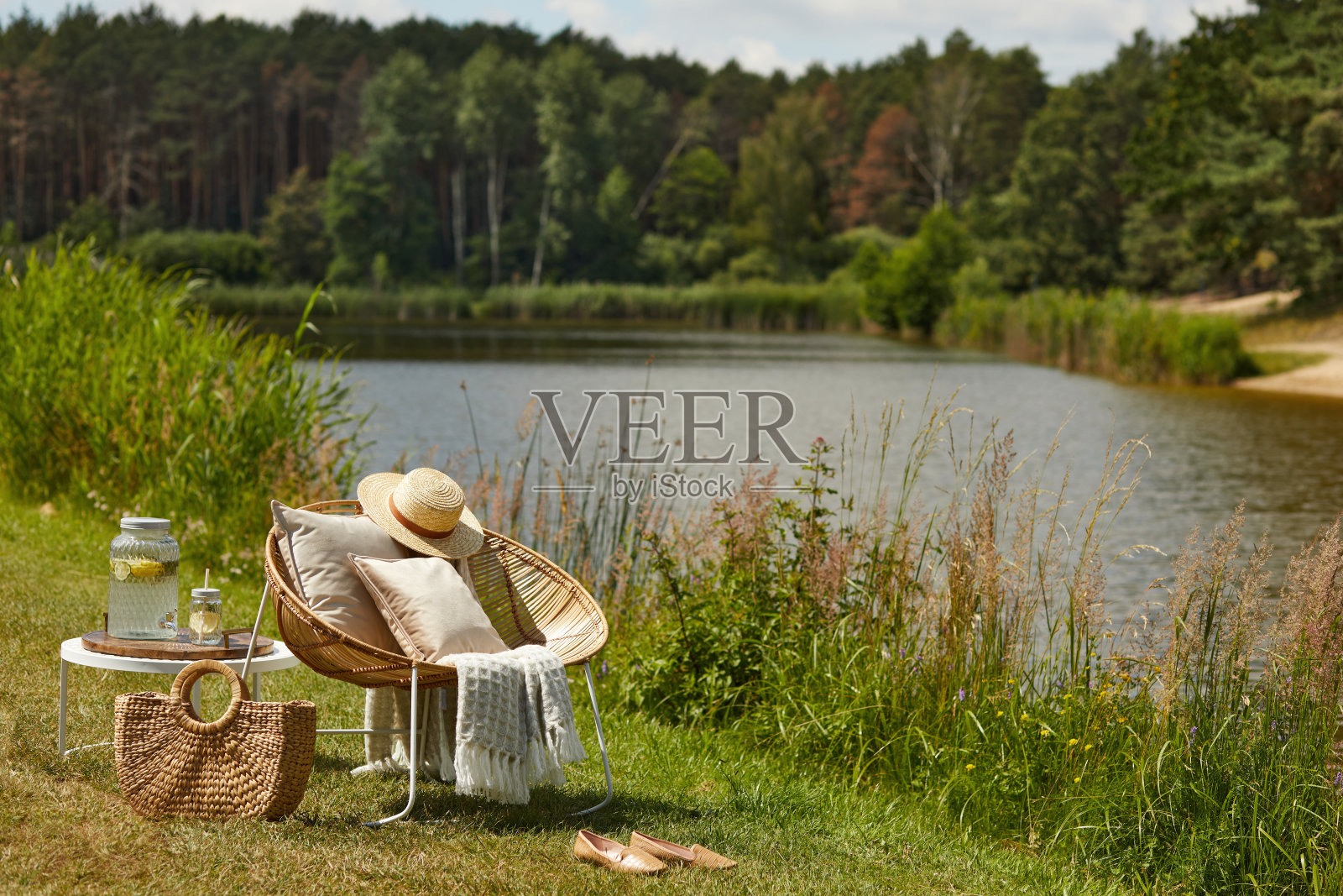 造型时尚的户外湖上花园配有设计藤扶手椅、咖啡桌、格子椅、靠枕、饮品等优雅配饰。夏天里的情绪。照片摄影图片