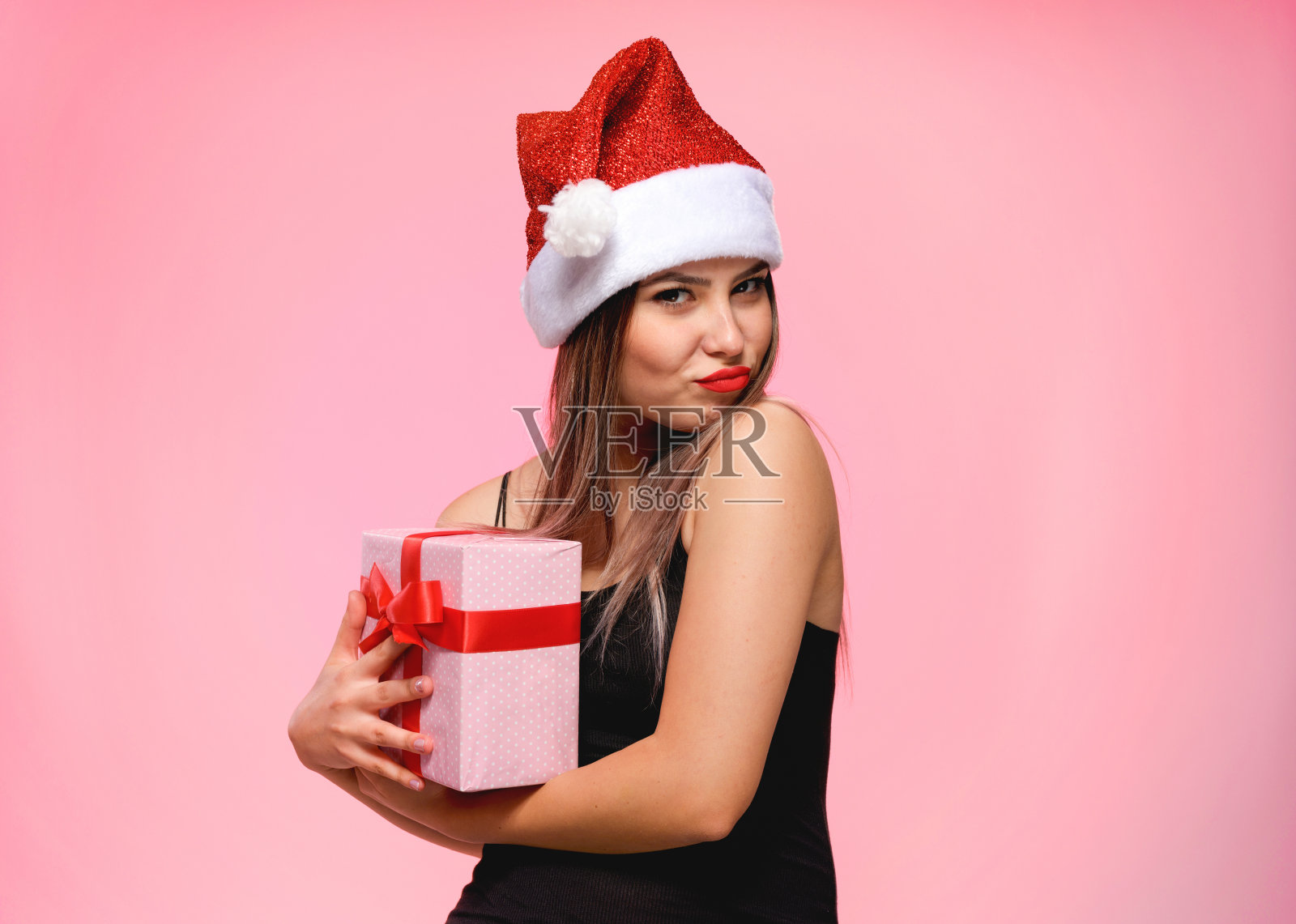 一个年轻美丽的女人的肖像与圣诞老人的帽子拿礼物，新年的概念照片摄影图片