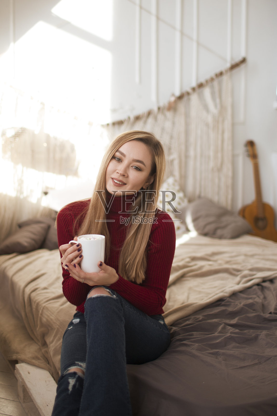 快乐的年轻女子喝咖啡或茶与圣诞礼物在家卧室。圣诞节早晨的概念。快乐的寒假。Hygge概念。照片摄影图片