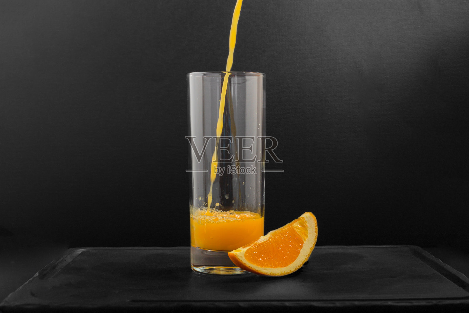 一个透明的杯子里装满了鲜榨的橙汁，背景是黑色的，上面有一片橙子。照片摄影图片