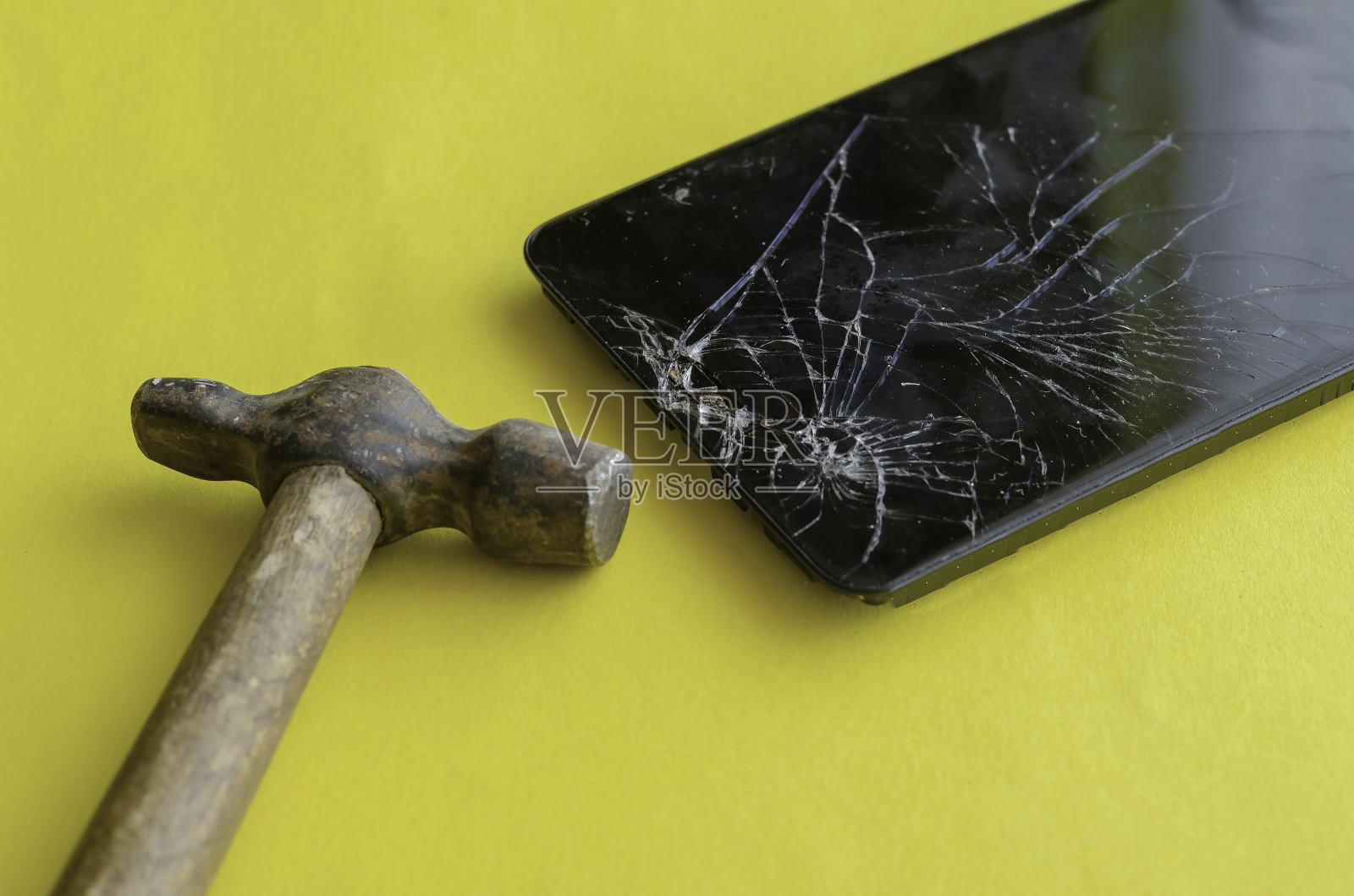 黄色背景上的黑色破手机和小锤子。照片摄影图片