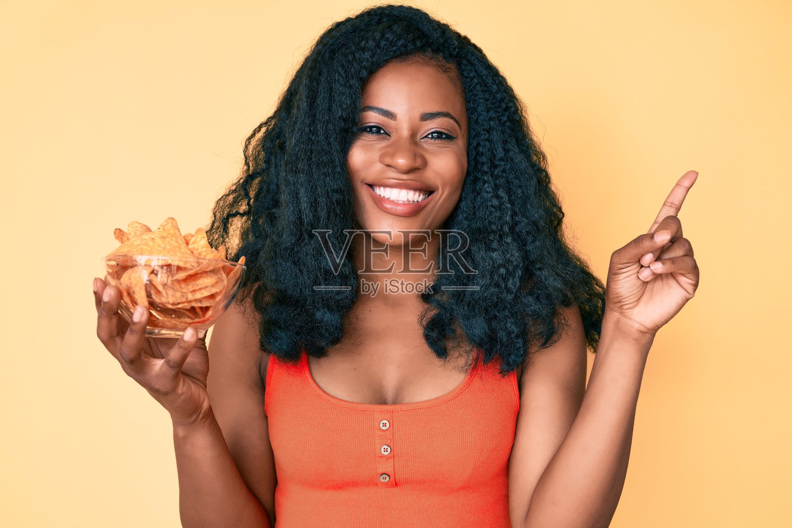 美丽的非洲女人拿着玉米片，土豆片微笑着幸福地指着与手和手指到一边照片摄影图片