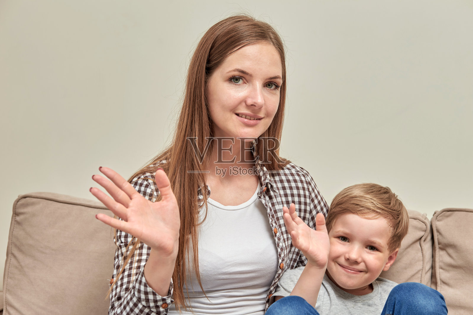 年轻漂亮的黑发妈妈拥抱她的儿子，他们一起挥手打招呼。照片摄影图片