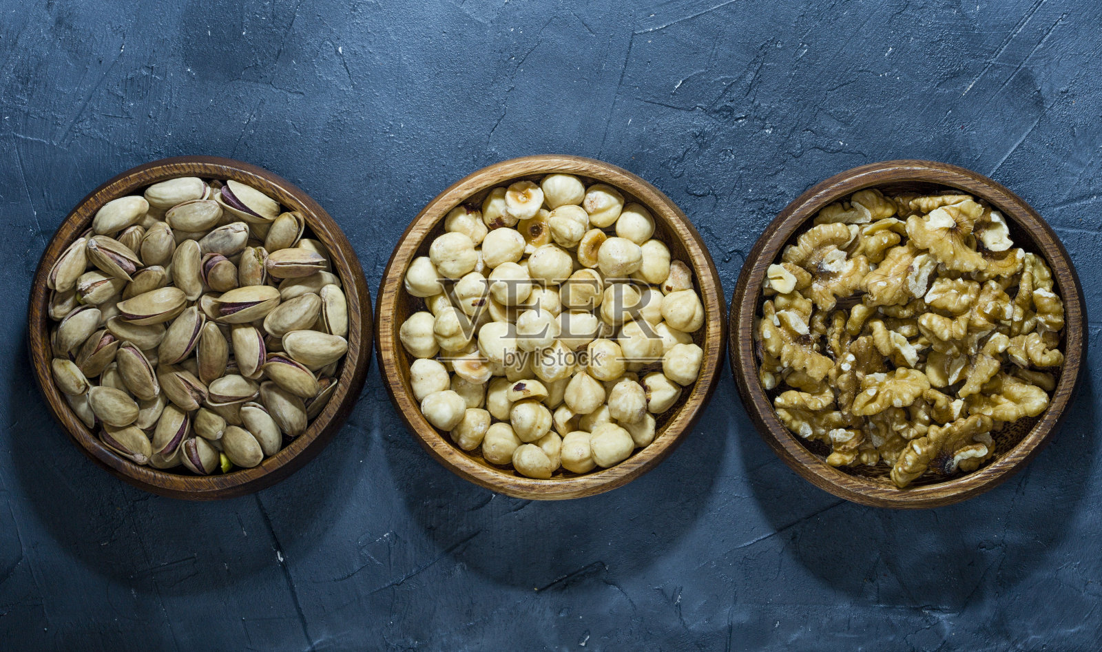 开心果，榛子和胡桃木碗特写在黑色的背景照片摄影图片