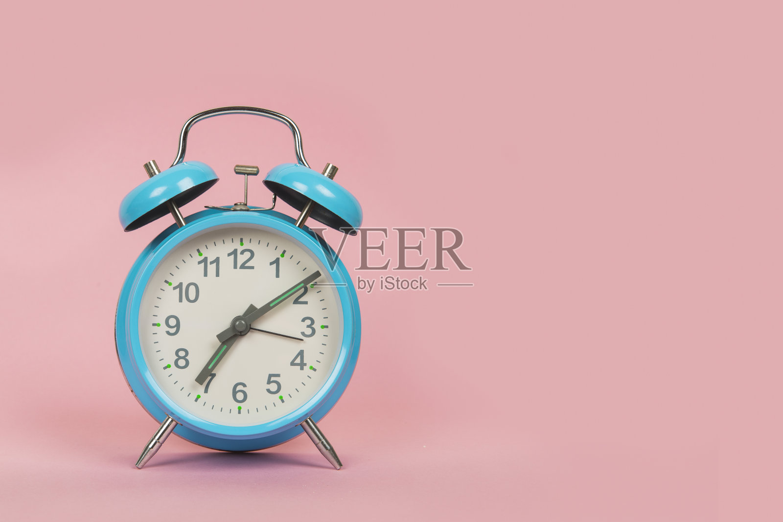 粉色背景上的蓝色古董闹钟，时间是7点10分照片摄影图片