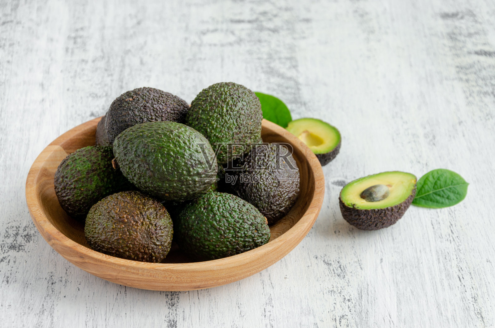 新鲜成熟的鳄梨和叶子放在木盘子里，木背景。健康食品的概念。副本的空间。照片摄影图片