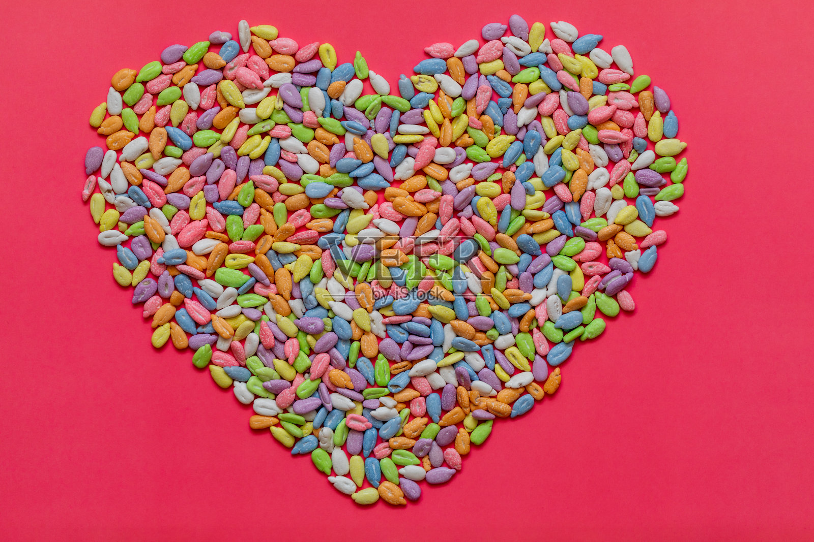 葵花籽在彩色釉上，在粉红色的背景上铺成心形。复活节，平铺，拷贝空间，俯视图。照片摄影图片