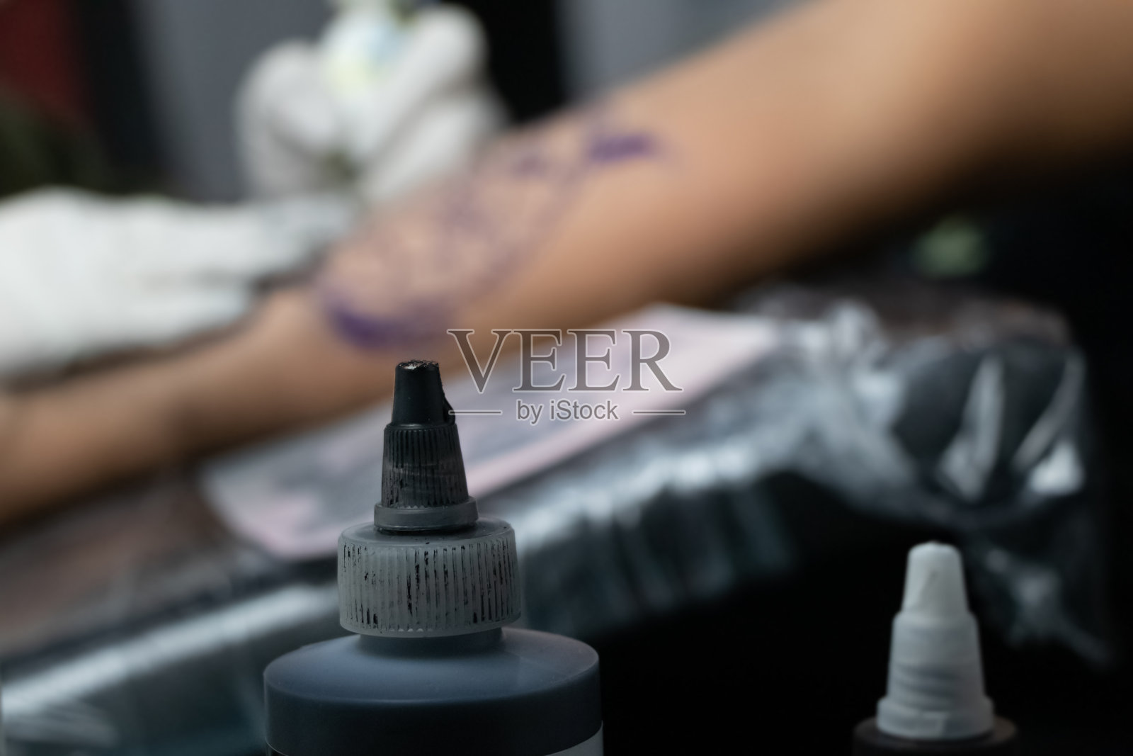 纹身的概念。一罐用于纹身的颜料，以一个男人的手为背景。你还可以看到大师是如何在前臂上填充图案的。照片摄影图片