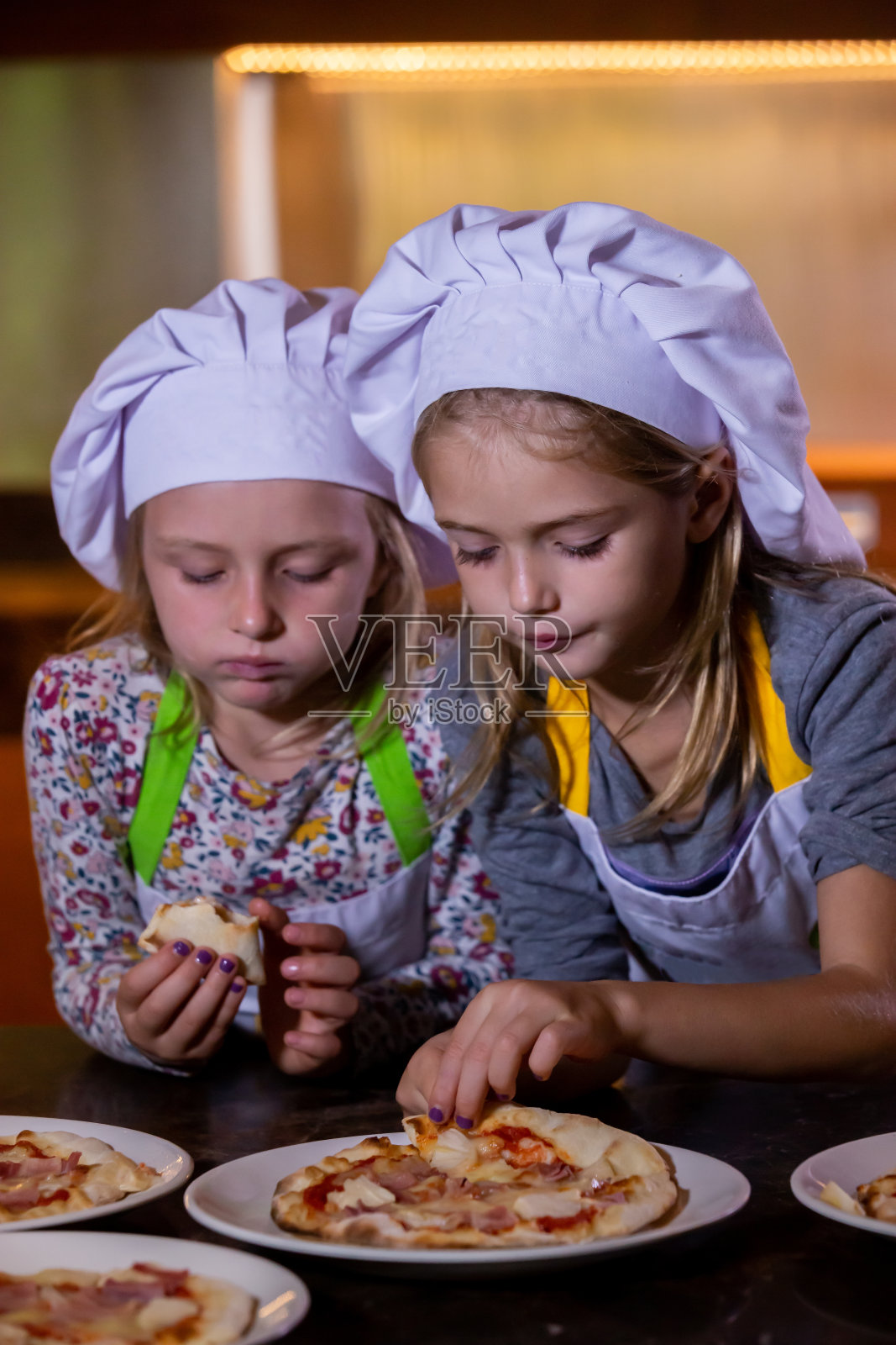 两个戴厨师帽的小女孩在烹饪大师课后吃披萨照片摄影图片