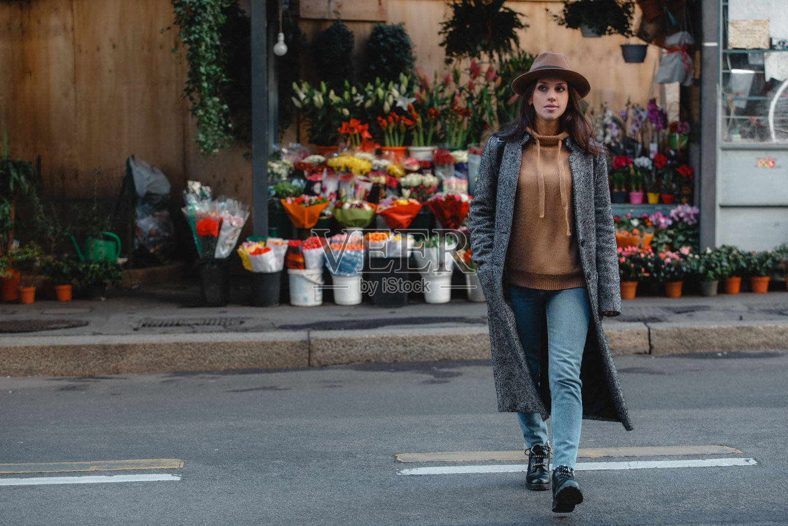 年轻美丽的女孩游客穿过马路，背景是一个美丽的购物帐篷与鲜艳的鲜花。照片摄影图片
