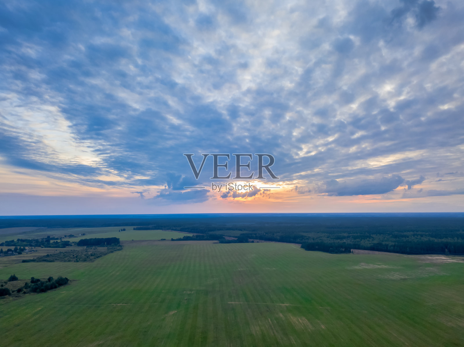 飞过美丽的绿色森林和田野在乡村日落。树木和田野的顶视图，美丽的天空在日落。四轴飞行器的照片照片摄影图片