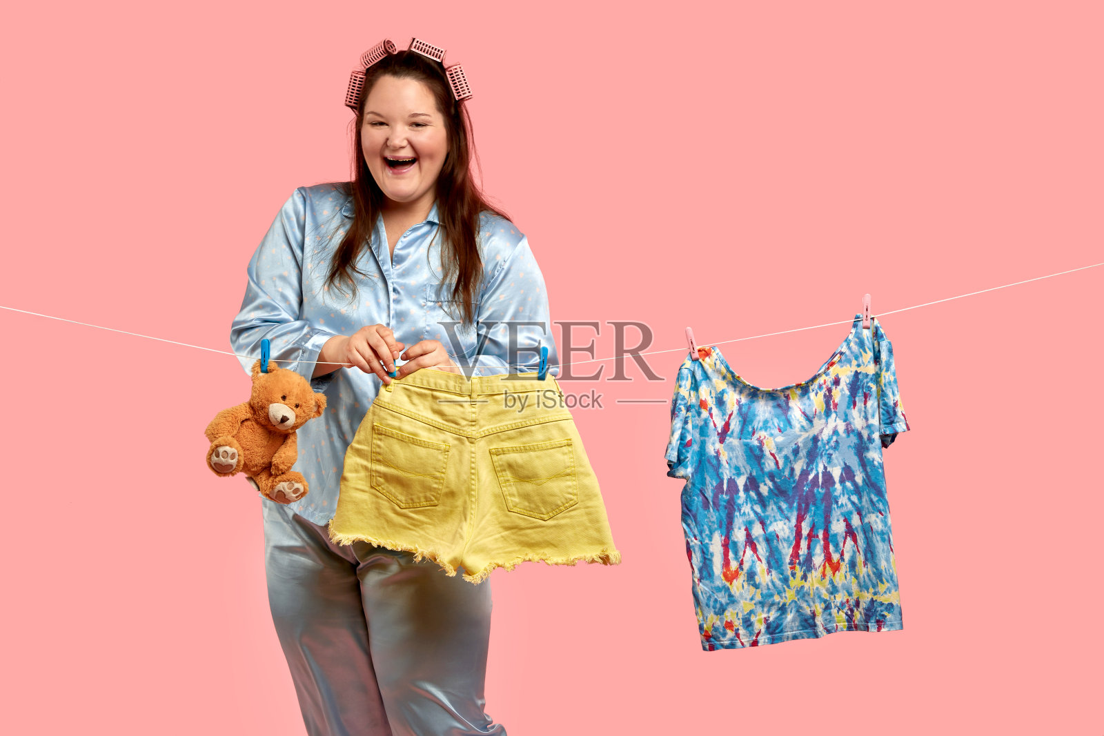 快乐的胖妻子，一个家庭主妇把洗好的衣服和玩具挂在绳子上。照片摄影图片