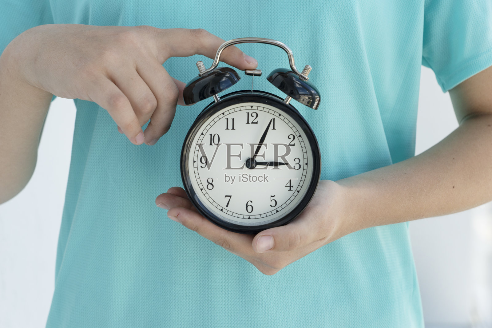 年轻女子的双手抱着圆圆的黑色闹钟。照片摄影图片