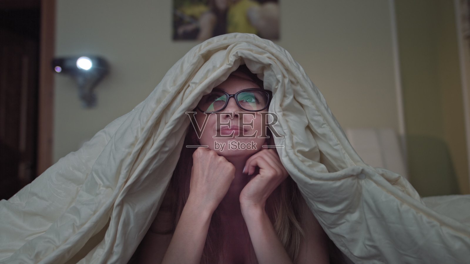 女人在家看喜剧，女孩躺在床上盖着毯子照片摄影图片