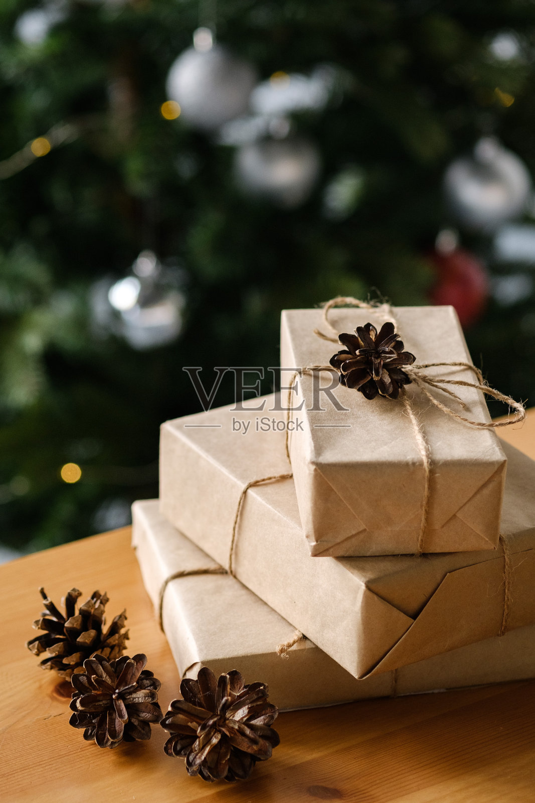 用手工包装的圣诞礼物放在木桌上，背景是一棵装饰过的圣诞树。圣诞节和新年的概念。照片摄影图片