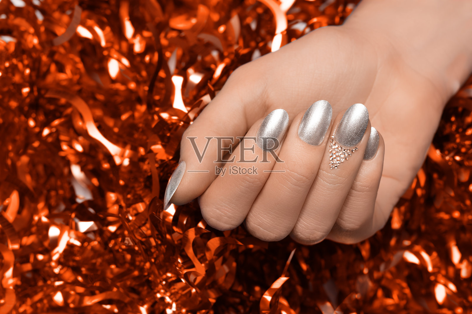 女性的手与圣诞钉子设计。银色指甲油修指甲。女性的手在橙色新年金丝背景。照片摄影图片