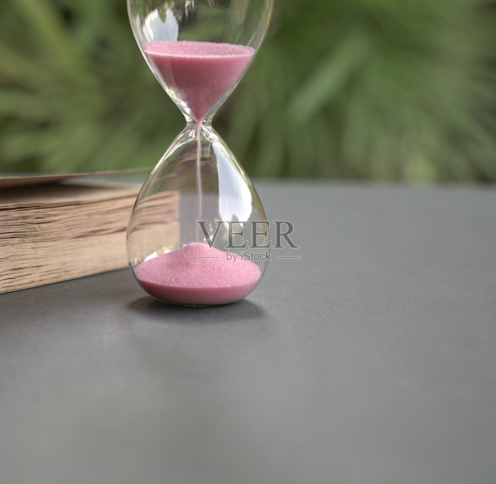 沙漏边流着沙子，旁边放着一本书。关闭了。时间管理的概念。照片摄影图片