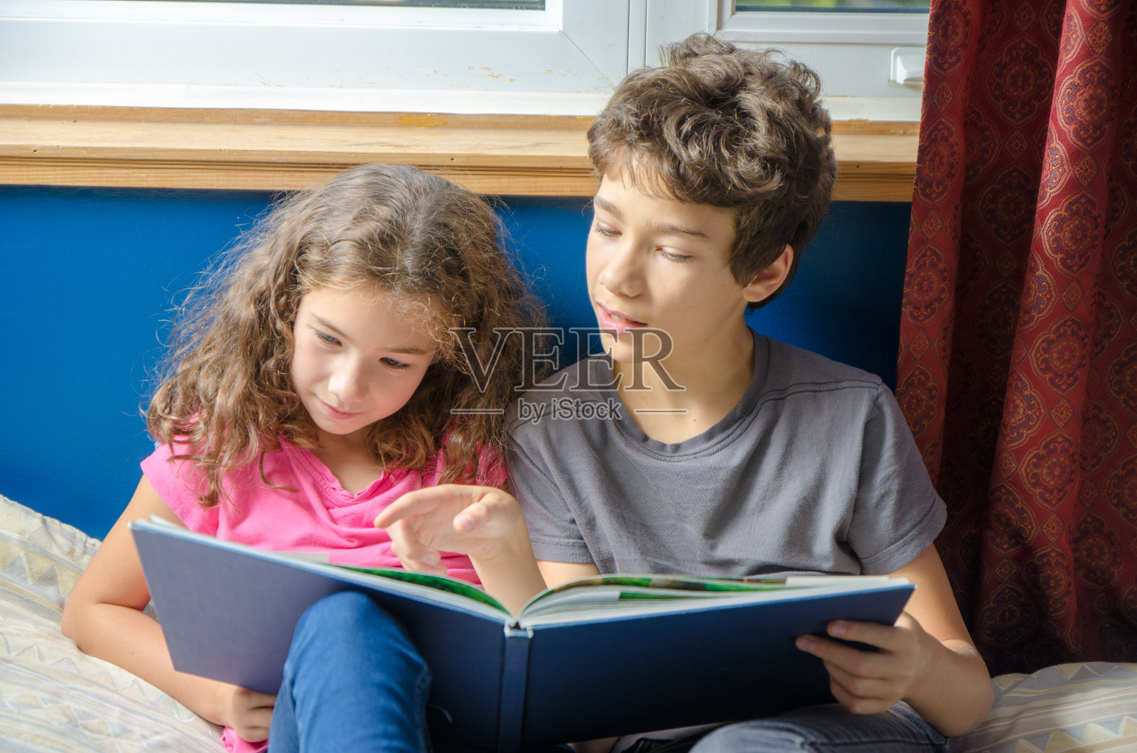 年轻的女孩和男孩在她的床上看书照片摄影图片