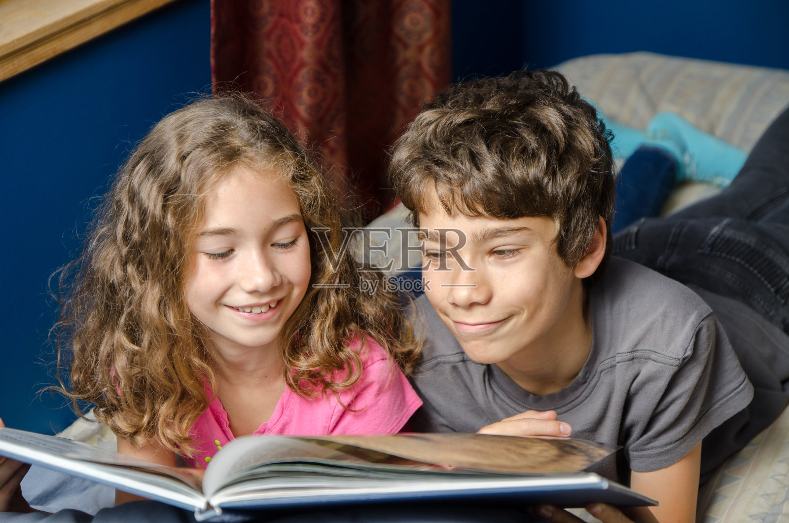 年轻的女孩和男孩在她的床上看书照片摄影图片