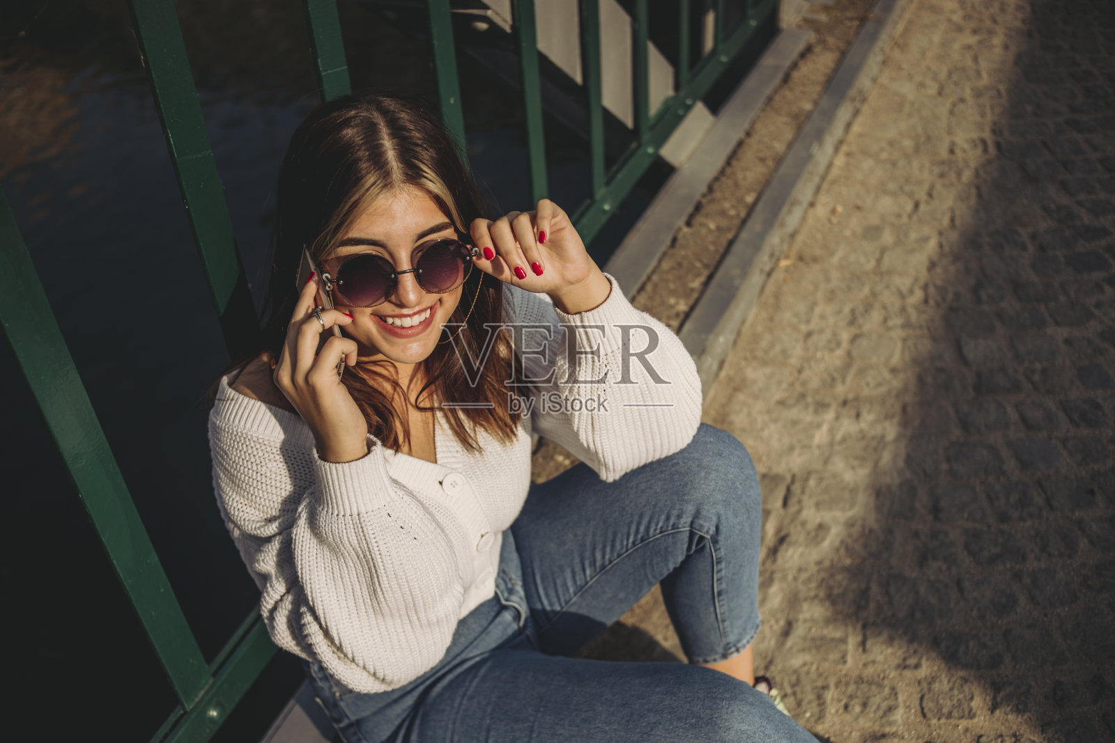 一个时髦的年轻女孩正坐在城市的一座桥上用手机休息照片摄影图片