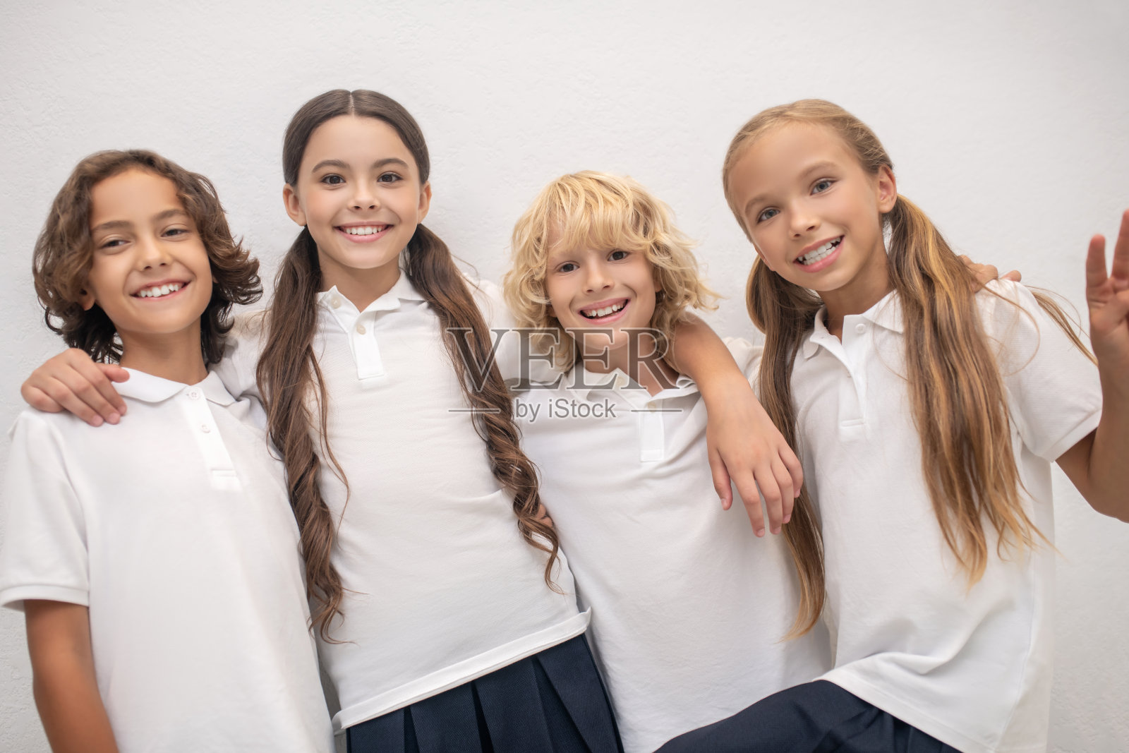 小学生们站在墙边，高兴地拥抱着照片摄影图片