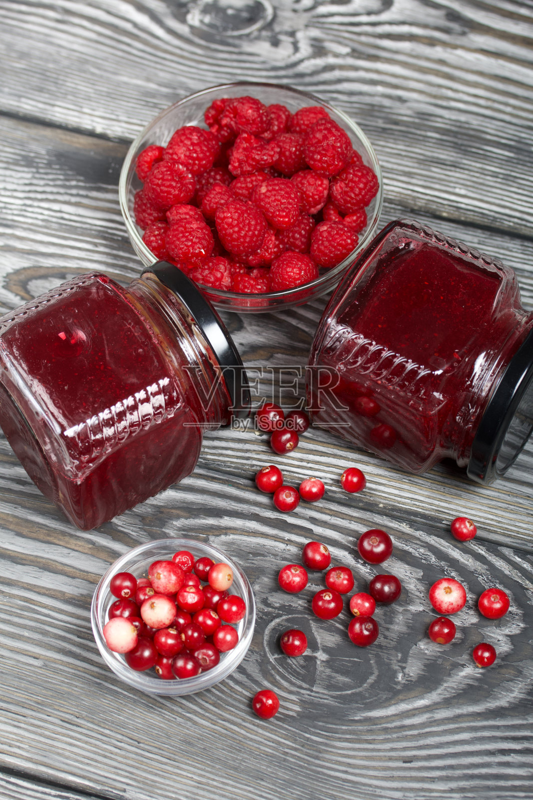 玻璃罐里的蔓越莓果酱。旁边是容器里的蔓越莓和覆盆子。一些浆果撒在表面上。在纹理优美的木板上。照片摄影图片