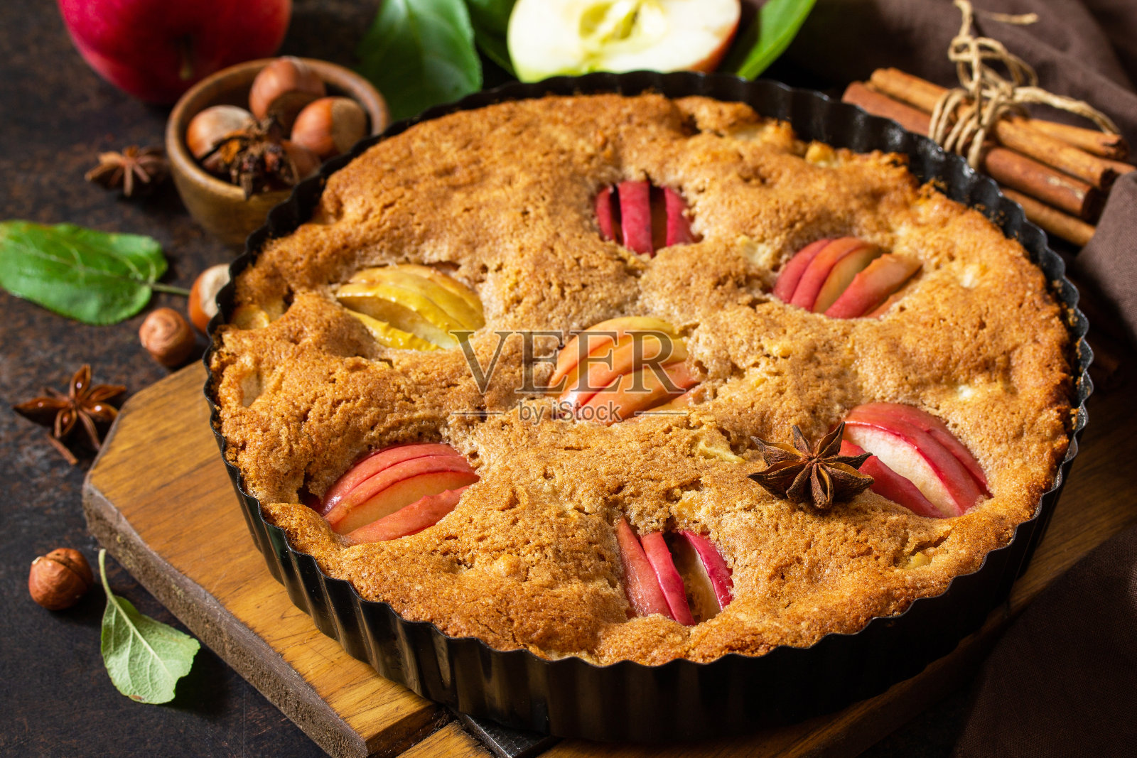 苹果烤季节性。质朴的木桌上放着带榛子和肉桂的苹果派。照片摄影图片