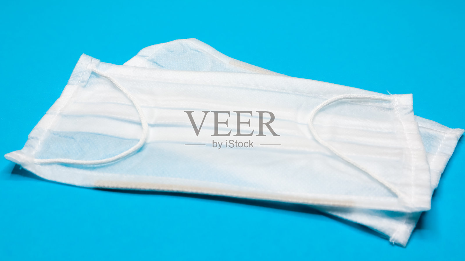 两个三层一次性外科口罩，用橡胶垫盖住口鼻，以蓝色背景。防护细菌、保健和医药的概念。新型冠状病毒肺炎照片摄影图片