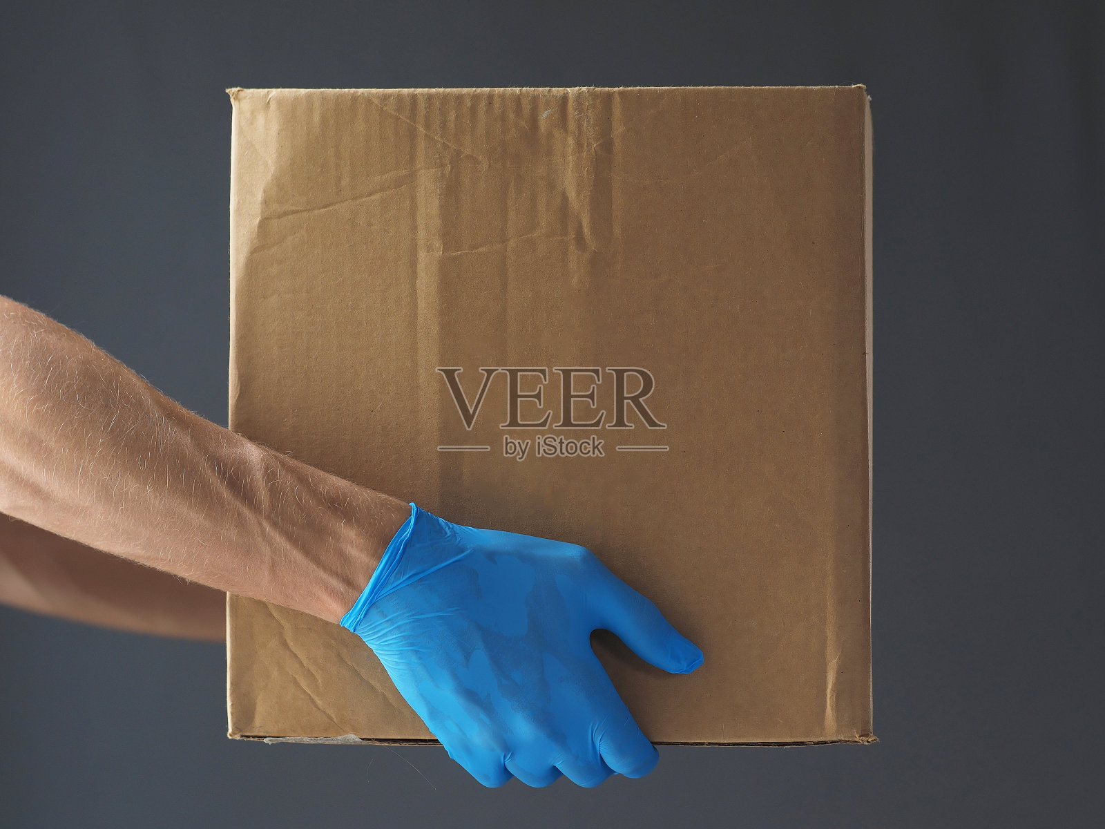 特写镜头。一名男子戴着蓝色手套送纸板箱。照片摄影图片