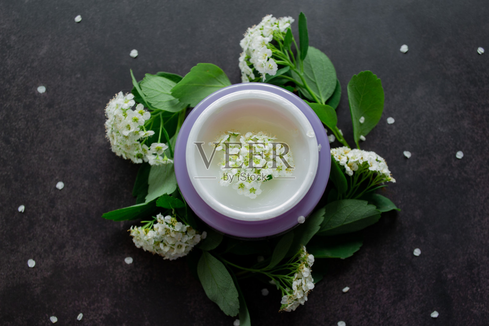 瓶身为淡紫色，白色奶油色，质地细腻，里面有白色的花朵。绣线菊枝叶茂盛，到处都是。暗的背景照片摄影图片