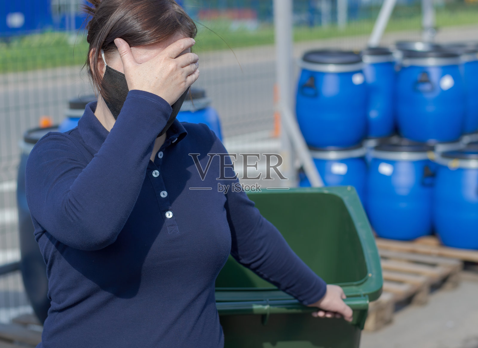 一个戴面具的女人拿着一个大塑料罐里的东西，遮住了她的脸。照片摄影图片