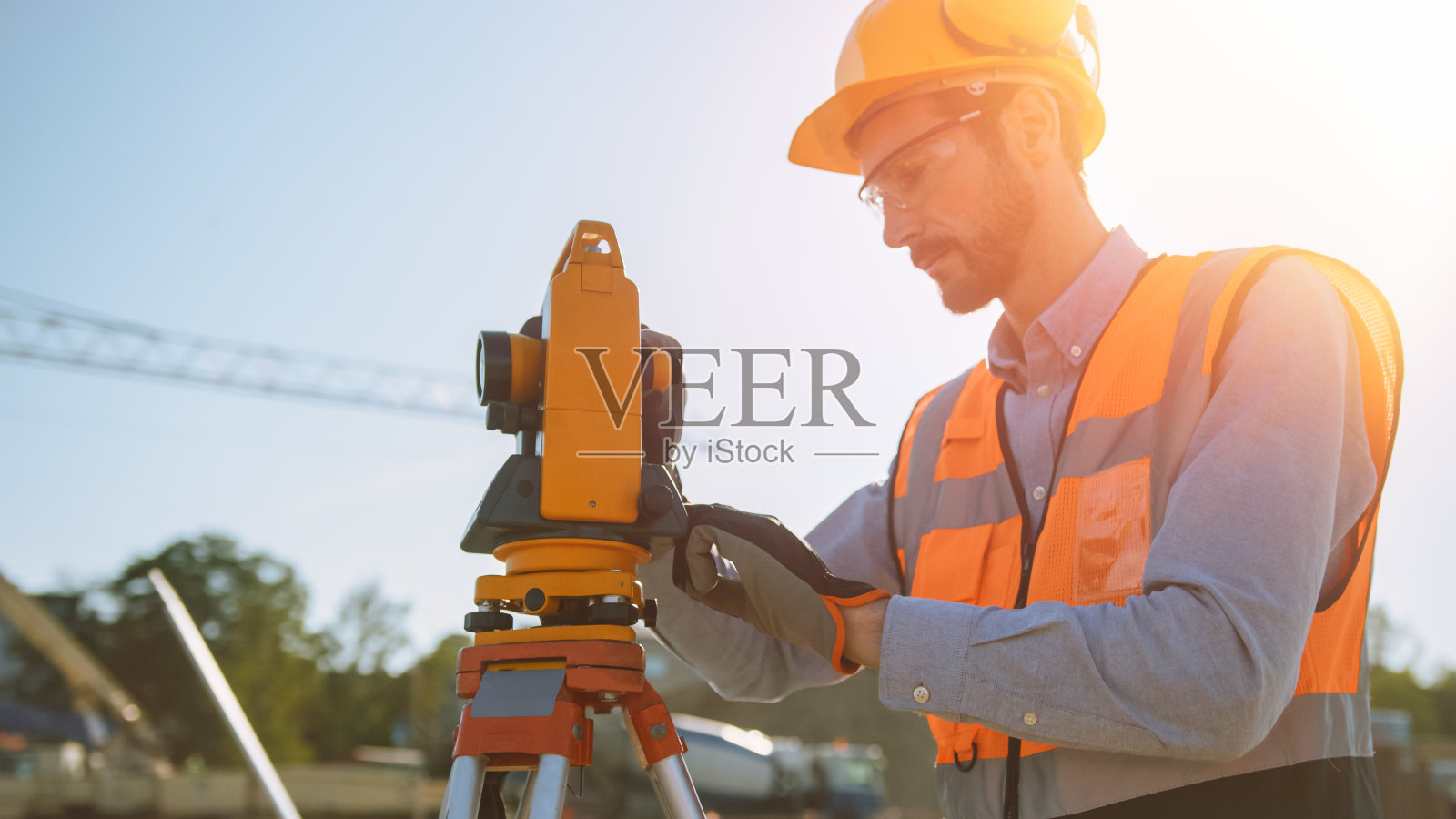 建筑工人使用经纬仪测量光学仪器在施工现场测量水平面和垂直面角度。戴安全帽的工人正在为大楼做投影。照片摄影图片