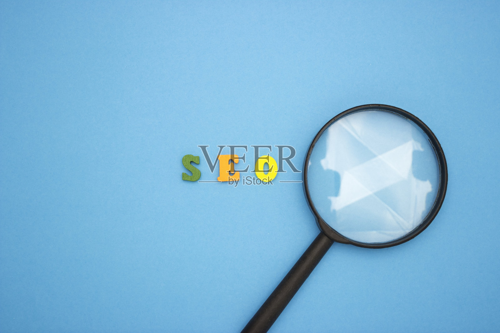 单词SEO在一个蓝色背景的木制多色字母。附近的放大镜。照片摄影图片