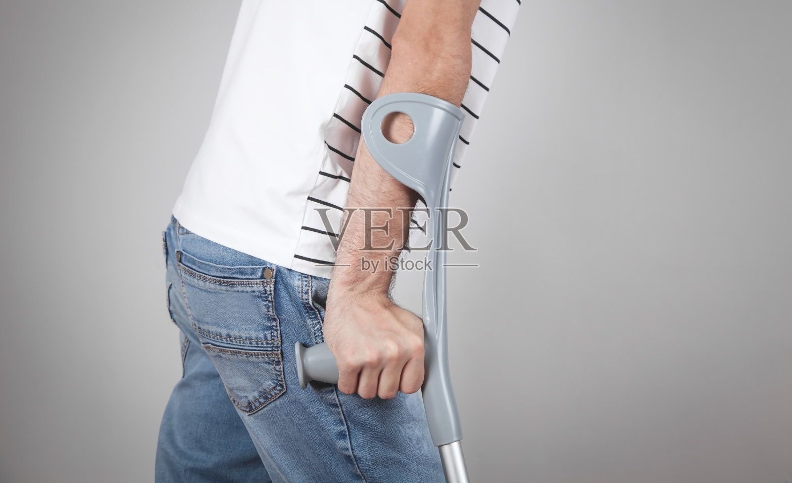 灰色背景上拄着拐杖的白人男子。照片摄影图片