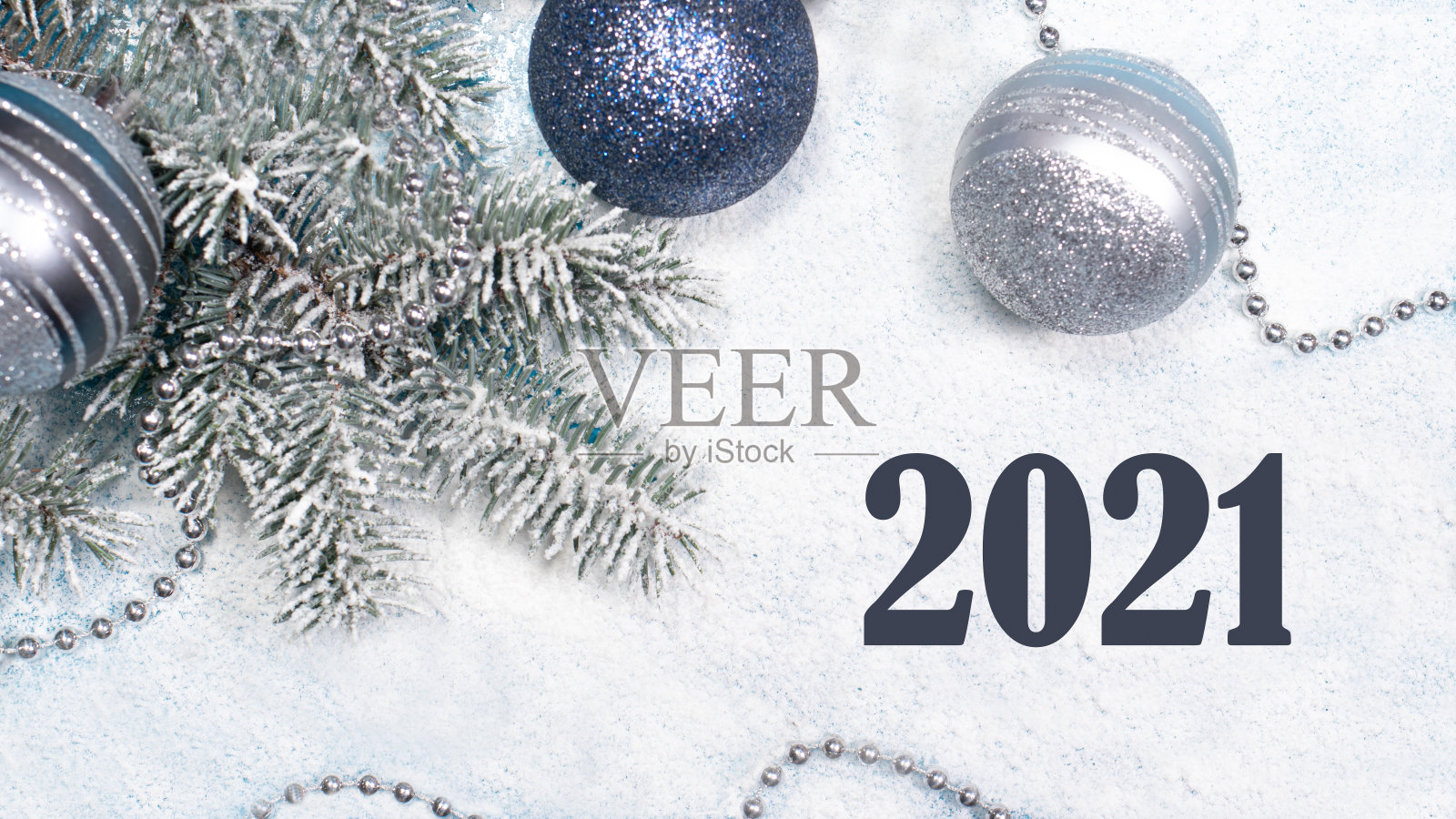 在白雪覆盖的白色背景上，云杉树枝上挂着圣诞玩具和珠子，上面写着“2021”。节日卡片。照片摄影图片