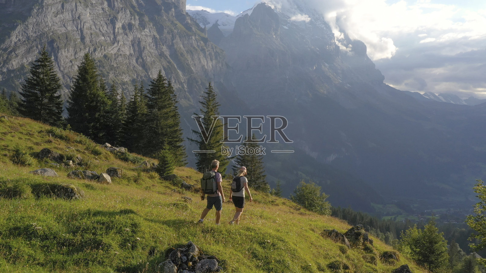 鸟瞰图的徒步旅行夫妇穿越高山草地，在日出照片摄影图片