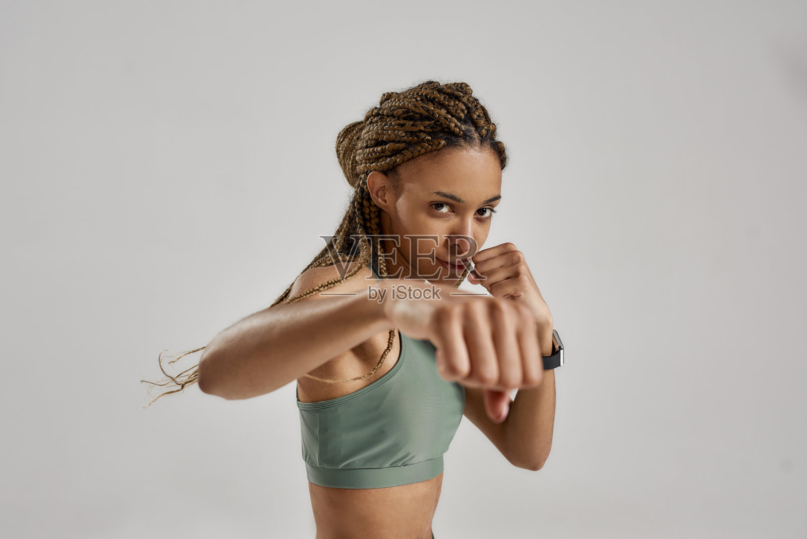 刻苦训练。年轻的肌肉美丽的混合种族的女人，女拳击手看着相机和拳头，而站在孤立的灰色背景照片摄影图片