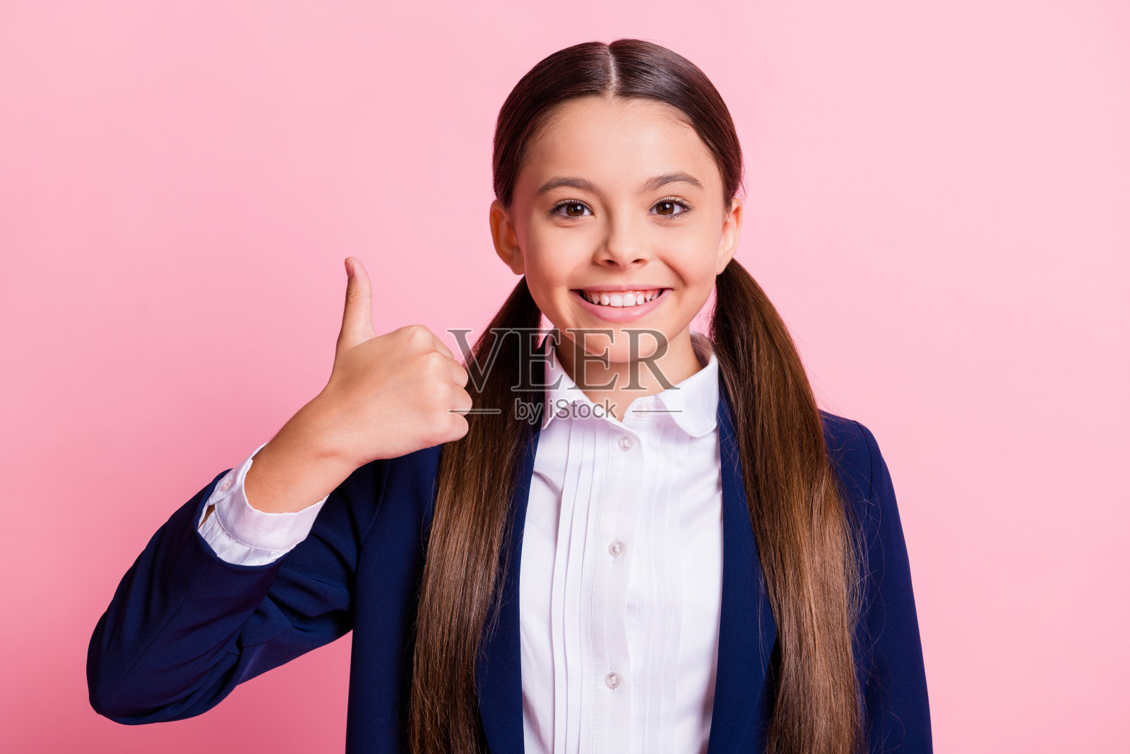 她的特写，她漂亮迷人，开朗愉快，自信的女孩显示拇指，推荐交易做广告，选择选择孤立的粉色柔和的颜色背景照片摄影图片